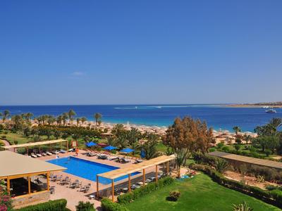 View of a hotel pool with palm trees and sea view under a clear sky.