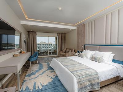 Modern hotel room with double bed, desk, seating area, and balcony access.
