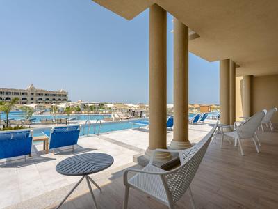 Modern terrace with seating overlooking pool and hotel building under clear sky.