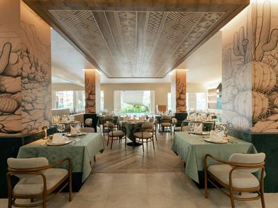 Modern restaurant with green tablecloths, wooden furniture, and wall art in a hotel.