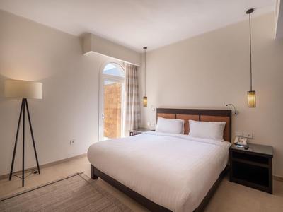 Simple hotel room with double bed, nightstand, floor lamp, and access to balcony or terrace.