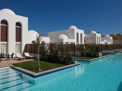 Modern hotel complex with a clear blue pool, white buildings, and dark wood accents under a clear sky.