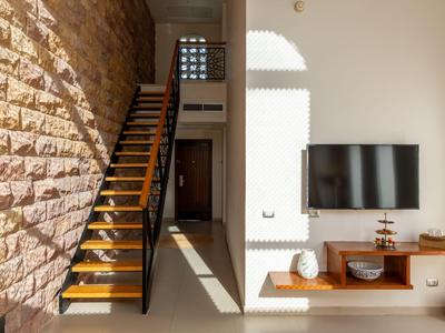 Modern living space with wooden stairs, stone wall, and wall-mounted TV in bright light.