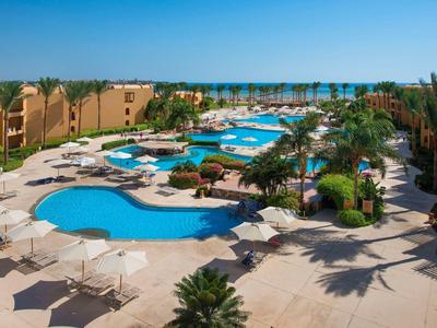 Obszar basenu hotelowego z wieloma basenami, palmami i leżakami pod jasnym niebieskim niebem.