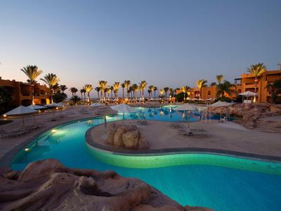 Večerní bazén s palmami a lehátky v hotelovém resortu.