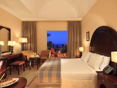 Przytulny pokój hotelowy z dużym łóżkiem, miejscem do siedzenia i nocnym widokiem na miasto.