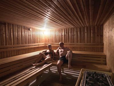 Dwie osoby relaksują się w drewnianej saunie z ciepłym oświetleniem.
