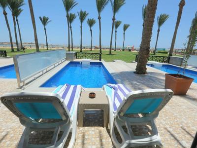 Widok na dwa leżaki obok prywatnego basenu z widokiem na morze i palmy.