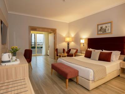 Elegant hotelkamer met groot bed, warm licht en balkon met uitzicht op zee.