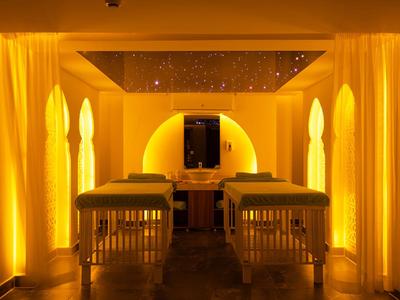Warm verlichte wellnessruimte met twee behandelbedden en gele gordijnen.