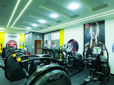 Moderne hotelgym met cardioapparatuur en felgele accenten op de muren.