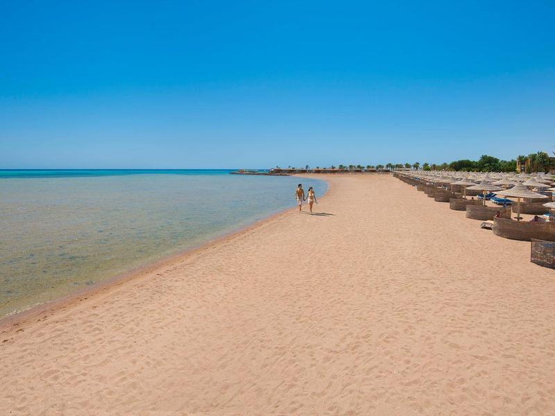 Długa piaszczysta plaża z czystą wodą i leżakami pod niebieskim niebem.