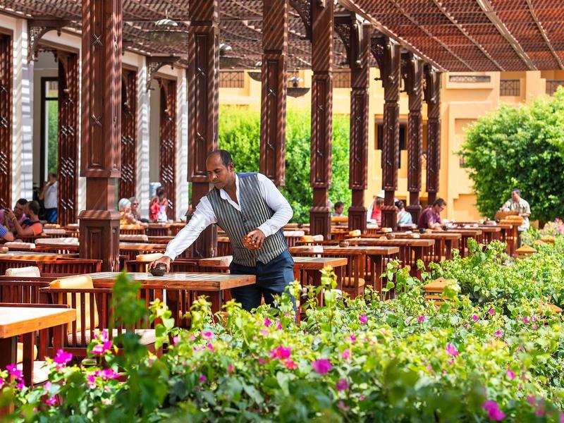Personel nakrywający stoliki w otwartej restauracji z drewnianymi kolumnami i zielonymi roślinami