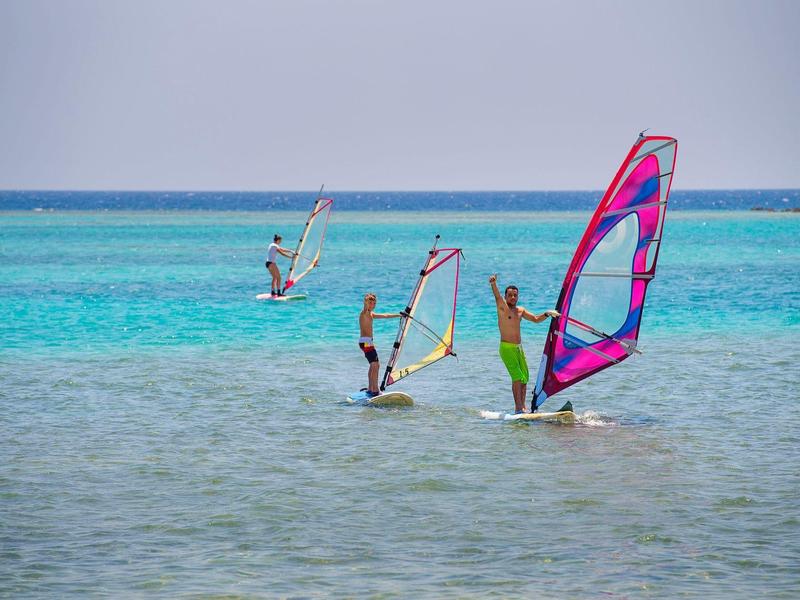Trzech windsurferów ślizga się po przezroczystej turkusowej wodzie w słoneczną pogodę.