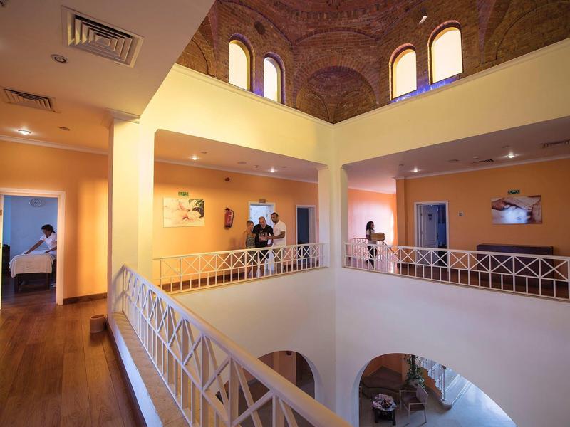 Wnętrze hotelu z otwartym atrium, balkonami i wysokimi sklepionymi sufitami.