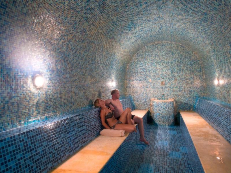 Para relaksuje się w pokoju spa pokrytym niebieskimi mozaikowymi płytkami z ławkami.