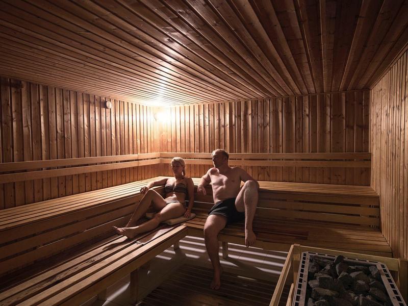 Dwie osoby relaksują się w drewnianej saunie z ciepłym oświetleniem.