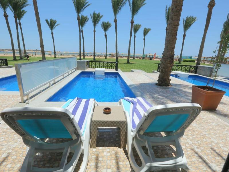 Widok na dwa leżaki obok prywatnego basenu z widokiem na morze i palmy.