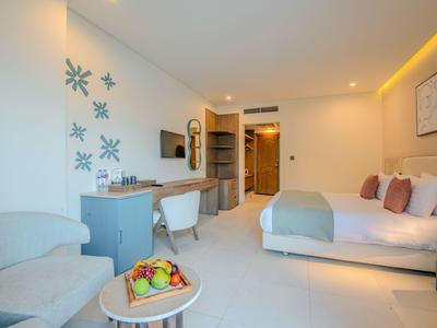 Helles Hotelzimmer mit Doppelbett, Sitzbereich, Schreibtisch und Obstkorb auf Tisch.