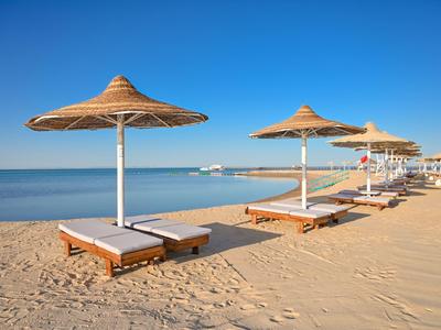 Leere Strandliegen mit Strohmachschirm an einem ruhigen sonnigen Strand.
