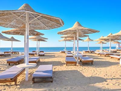 Sandstrand mit Sonnenliegen und Strohhut-Sonnenschirmen unter blauem Himmel