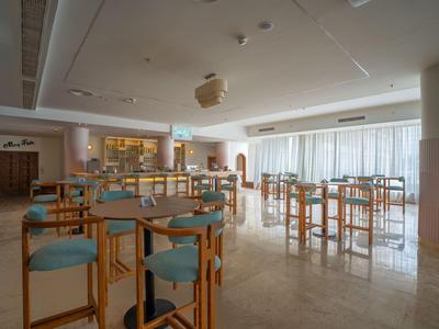 Área de comedor moderna y luminosa con sillas de madera, mesas y grandes ventanas en un hotel.