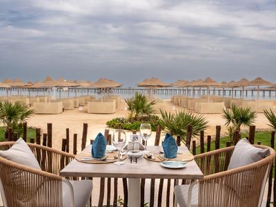 Mesa puesta con servilletas azules en la playa con sombrillas y palmeras.
