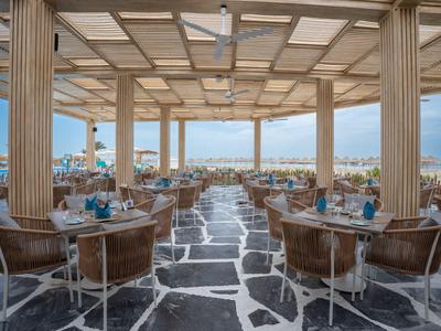 Restaurante al aire libre con sillas de mimbre y vista al mar bajo un techo de madera.