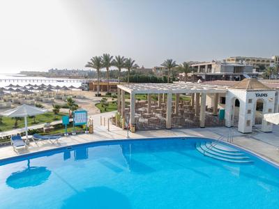 Large blue hotel pool with sun umbrellas, palm trees, and hotel buildings in the background.