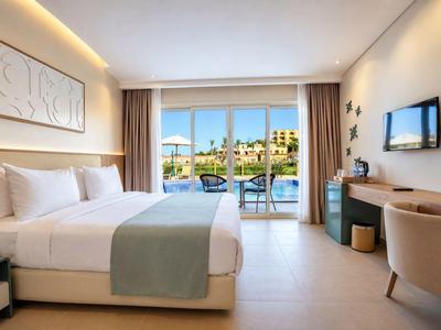Modernes Hotelzimmer mit Doppelbett, Balkon und Blick auf Pool und Garten.