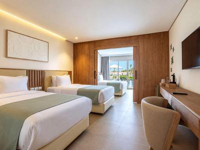 Modernes Hotelzimmer mit zwei Einzelbetten, Schreibtisch und Blick auf Balkon und Meer.