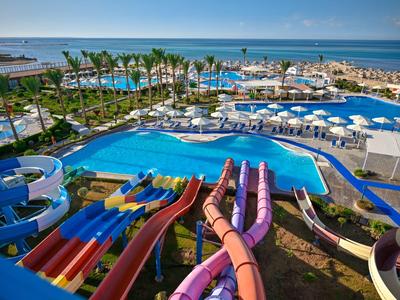 Varias toboganes acuáticos coloridos conducen a una gran piscina con sombrillas y vista al mar.