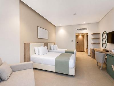 Modern hotel room with two single beds, sofa, desk, and TV.