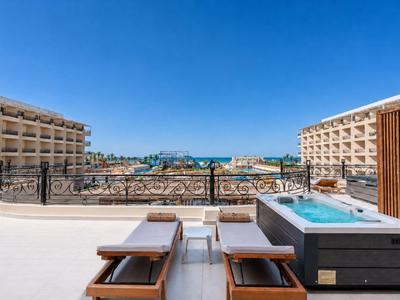 Hotel terrace with sun loungers, hot tub, and view of the sea and blue sky.