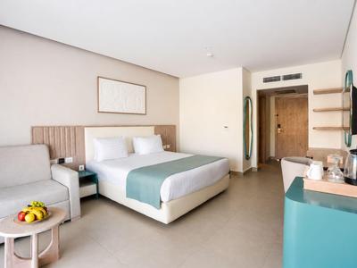 Bright hotel room with double bed, sofa, small table, and modern furnishings.