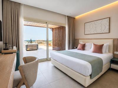 Bright hotel room with double bed, desk, and terrace overlooking the sea.