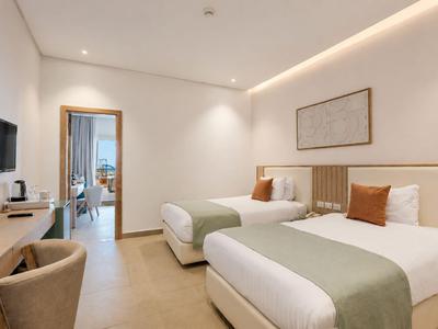 Modern hotel room with two single beds, desk, and wall-mounted TV.