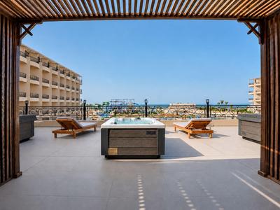 Terrace with sun loungers overlooking the seaside promenade under a clear sky.