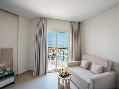 Habitación de hotel luminosa con sofá, mesa y balcón con vista a la piscina.