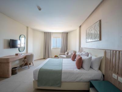 Habitación de hotel moderna con dos camas grandes, escritorio, silla y ventana con cortinas claras.