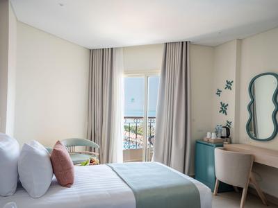 Habitación de hotel luminosa con cama, silla, escritorio y balcón con vista al mar.