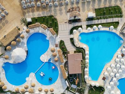 Vista aérea de dos piscinas azul claro con tumbonas y sombrillas blancas en los bordes.
