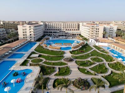 Gran complejo hotelero con varias piscinas, césped verde y sombrillas bajo un cielo despejado.