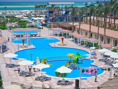 Großer Hotelpool mit Wasserrutschen und Sonnenschirmen neben dem Meer.