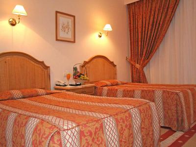 Hotel room with two single beds, wooden headboards, patterned bedspreads, and warm lighting.