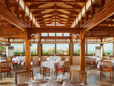 Světelná restaurace s dřevěnými stropy a prostřenými stoly s výhledem na moře.