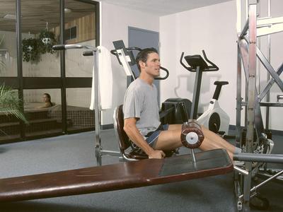 Muž cvičí na stroji na natahování nohou v posilovně s fitness vybavením.