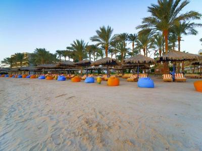Strand mit Sand, bunten Sitzsäcken und Palmen unter klarem Himmel am frühen Abend.