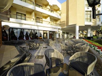 Venkovní terasa hotelu s stolky a židlemi vedle květinového záhonu.