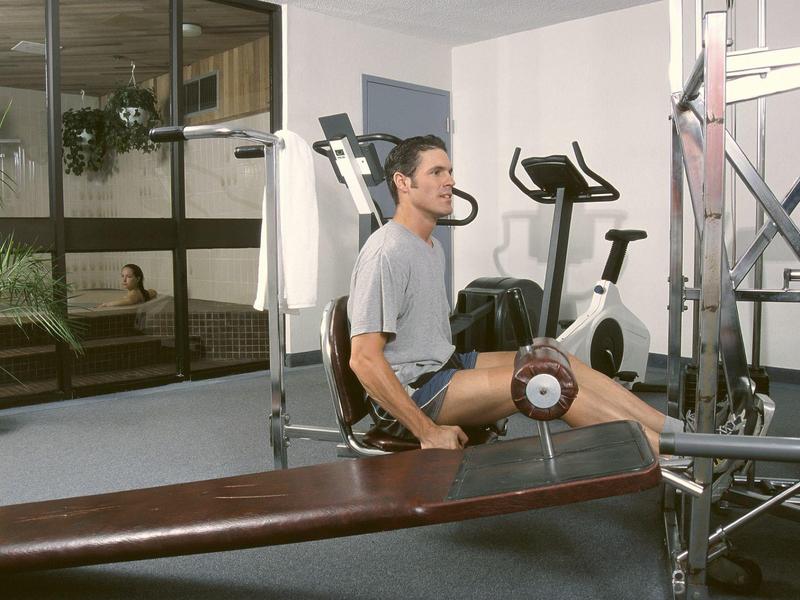 Mann trainiert mit Beinmaschine im hellen Fitnessraum mit großen Fenstern und Pflanzen.